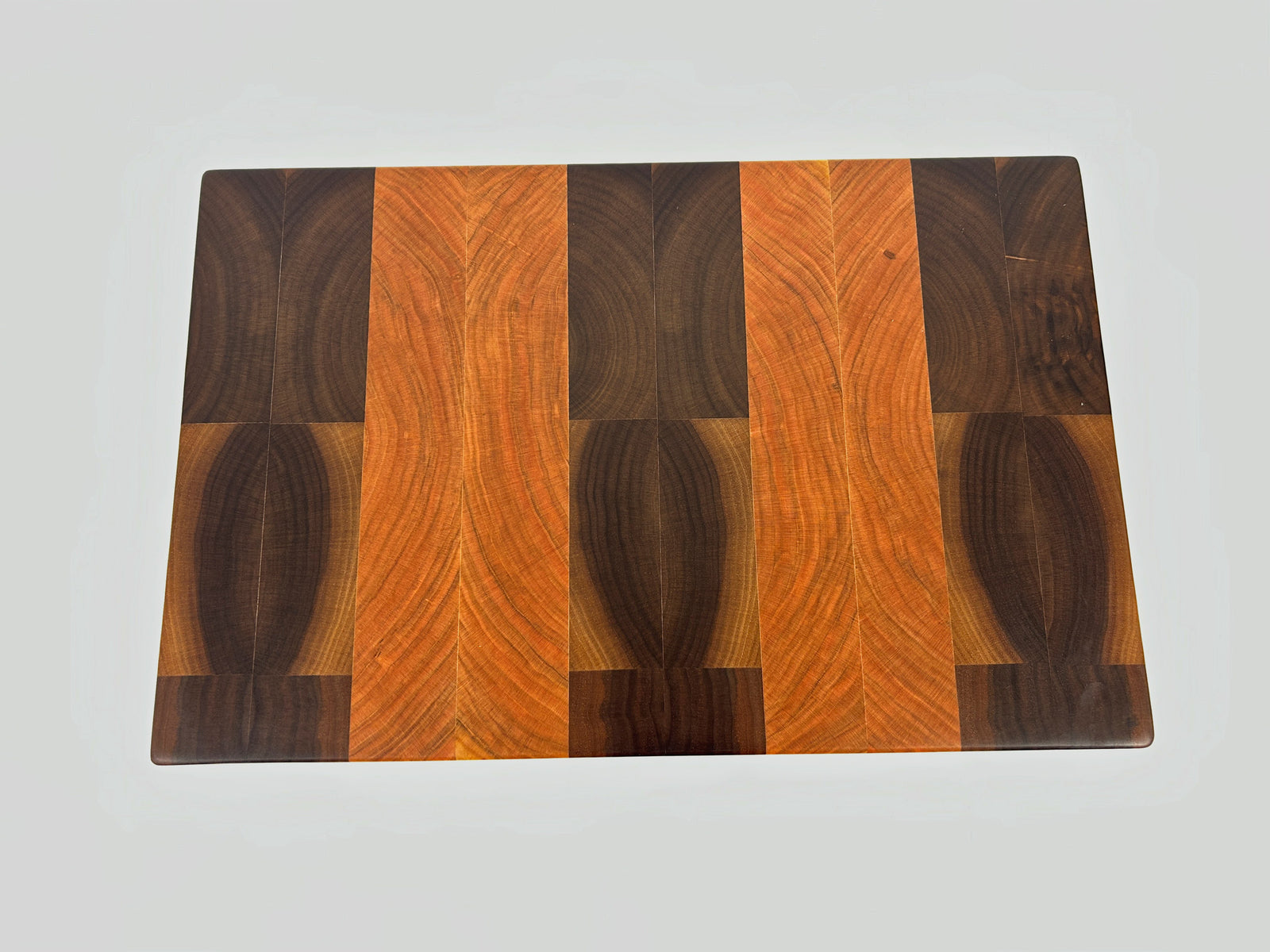 End grain cherry and walnut cutting board with a distinct striped pattern on a white background