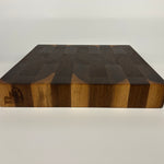 End-grain walnut cutting board with a dark brown and light brown pattern on a white background, side view