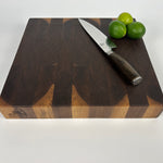 WEnd-grain walnut cutting board with a dark brown and light brown pattern with a knife and limes on a white background