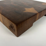 Thick walnut end-grain cutting board corner close-up view on white background, with unique grain pattern and underside handle visible