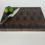 Thick, Walnut end grain cutting board with a knife and limes on a white background