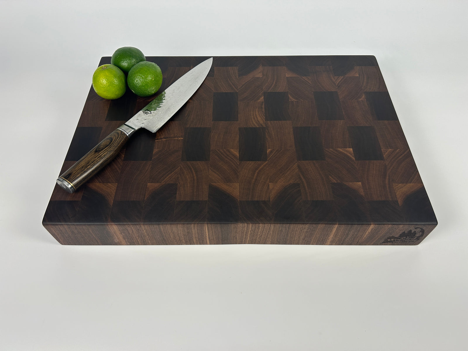Thick, Walnut end grain cutting board with a knife and limes on a white background