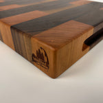 End grain Walnut and Cherry cutting board with a striped pattern on a white background, corner angle