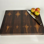 Thick End grain walnut cutting board with geometric heartwood and sapwood patterning, with a knife and apples on a white background