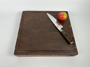 Walnut wood cutting board with a knife and an apple on a white background