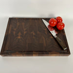 End grain walnut cutting board with geometric grain pattern and juice groove, top down view on white background with a knife and tomatoes on a white background