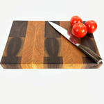End grain cherry and walnut cutting board with a distinct striped pattern with tomatoes and knife on top, on white background