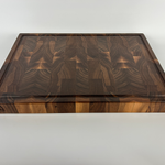 End grain walnut cutting board with geometric grain pattern and juice groove, side view on white background